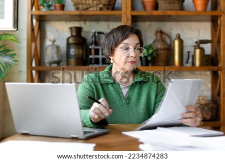 A mature woman during a document check. She checks the correctness of filling out the documentation and enters the data on the site. Modern technology in everyday life concept.