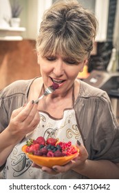 Mature Woman Eating Berry Fruit Salad In The Kitchen.