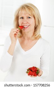 Mature Woman Eating A Bowl Of Strawberries And Smiling