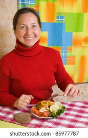 Mature Woman Eating Breaded Fish In Her Kitchen