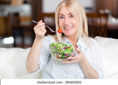 Mature Woman Eating A Healthy Salad On Her Sofa