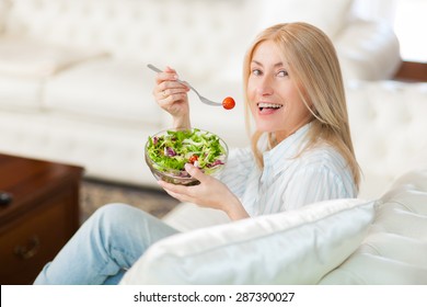 Mature Woman Eating A Healthy Salad On Her Sofa