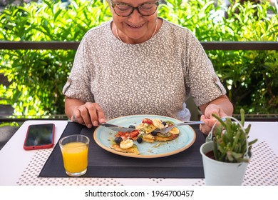 Mature Woman Eating Healthy Summer Breakfast, Classic American Pancakes With Banana, Kiwi, Fresh Berry And Honey