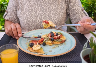 Mature Woman Eating Healthy Summer Breakfast, Classic American Pancakes With Banana, Kiwi, Fresh Berry And Honey