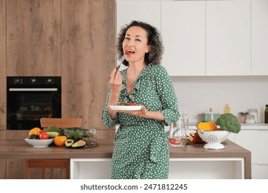 Mature woman eating vegetable salad in kitchen - Powered by Shutterstock