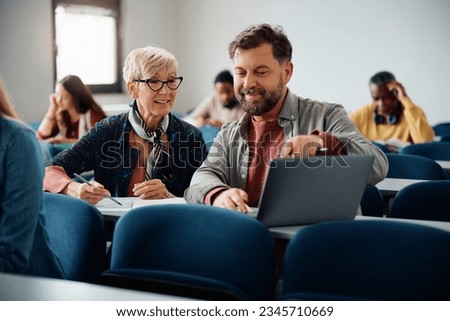 Mature woman e-learning on laptop with her classmate during a lecture in the classroom. 