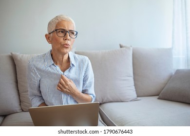 Mature Woman Experiencing Hot Flush From Menopause. Tired Mature Woman Tolerating Hot Flash. Hot Flashes. Exhausted Mature Woman Resting On Sofa And Having Hot Flash