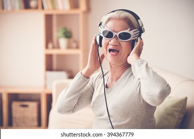 Mature woman in funny sunglasses  and headphones singing a song
