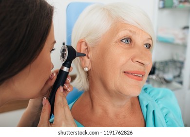 Mature Woman Getting Ear Exam At Clinic , Doctor Examining Elderly Patient Ear , Using Otoscope