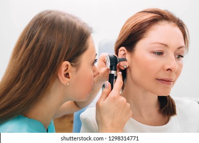 Mature Woman Getting Ear Exam At Clinic , Doctor Examining Patient Ear , Using Otoscope