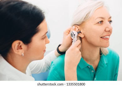 Mature Woman Getting Ear Exam At Clinic , Doctor Examining Patient Ear , Using Otoscope