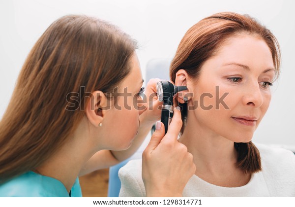 Mature woman getting ear exam at clinic ,\
doctor examining patient ear , using\
otoscope