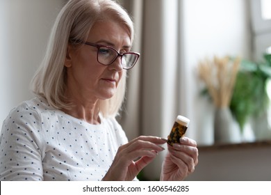 Mature Woman In Glasses Hold Bottle With Pills Read Medicine Instruction On Packaging Before Take Meds, Senior Female Retiree In Spectacles Thinking Of Medication Treatment, Elderly Healthcare Concept