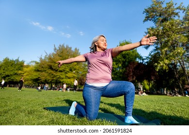 Mature Woman With Gray Hair Doing Yoga The Easy Version Of Warrior II Pose At An Urban Park