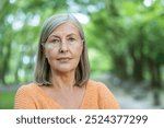 Mature woman with gray hair standing confidently in outdoor setting. Expressing calmness and wisdom. Sunny day adds warmth to the scene. Perfect representation of confidence and serenity in nature.