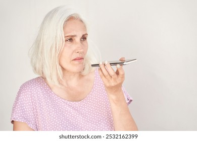 Mature woman with gray hair using smartphone voice assistant against plain background. - Powered by Shutterstock