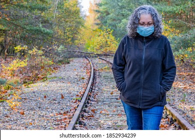 Mature Woman, Greyish Black Hair With Mask Walking Very Pensive On Disused Train Track, Old Iron Rhine Railway (IJzeren Rijn), Autumn Day In Meinweg Nature Reserve In Middle Limburg, Netherlands