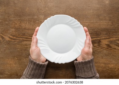 Mature woman hands holding white empty plate on dark brown wooden table background. Closeup. Point of view shot. Meal waiting concept. - Powered by Shutterstock