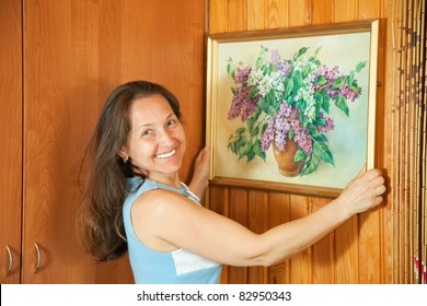 Mature Woman Hanging Art Picture On Wall At Home