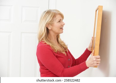 Mature Woman Hanging Picture On Wall