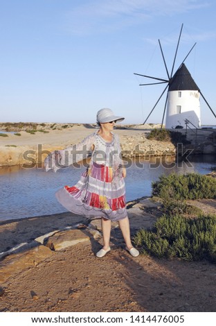 Mature woman, with hat playing with a handkerchief by the sea next to the salt flats and a mill in the Mar Menor, Murcia, Spain, pamela, holidays,
