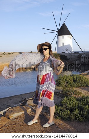 Mature woman, with hat playing with a handkerchief by the sea next to the salt flats and a mill in the Mar Menor, Murcia, Spain, pamela, holidays,