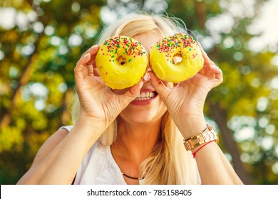 Mature Woman Having Fun Relaxing At The Park Hiding Her Face Behind Two Delicious Donuts With Glazing Playful Happy Emotional Expressive Food Snack Junk Dessert Sugar Diet Healthy Eating Cheat Meal