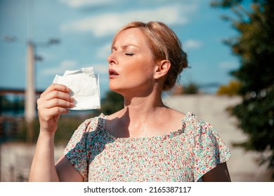 Mature Woman Having Hot Flashes Outdoors, Trying To Cool Herself With Paper Tissue. Blonde Female Portrait Cooling Down On Hot Summer Day