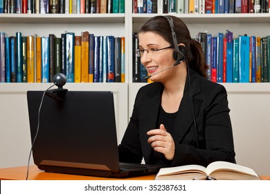 Mature Woman With Headset, Laptop And Webcam In Front Of A Lot Of Books, Giving Online Legal Advice Via A Video Call