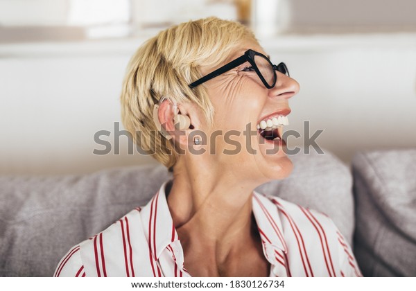Mature woman with\
hearing aid indoors\
smiling
