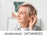 Mature woman with hearing aid in room