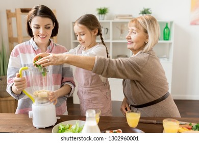 Mature woman and her granddaughter putting fresh green vegetables into blender while preparing smoothie for all family - Powered by Shutterstock