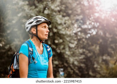 Mature Woman Hiker With Backpack And Sports Helmet Among Trees. Active Female Walking And Hiking In Extreme Terrain In Mountain Woods. Copy Space