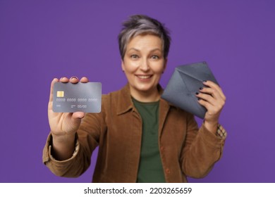 Mature Woman Hold Gift Card Hand With Fancy Dark Envelope. Happy Mature Woman Got Her New Bank Debit, Credit Card, Wearing Casual Isolated On Purple Background. Banking, Financial Concept. 