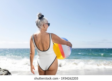 Mature woman holding a beach ball while in a swimsuit