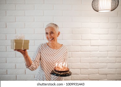 Mature Woman Holding A Birthday Cake And A Gift