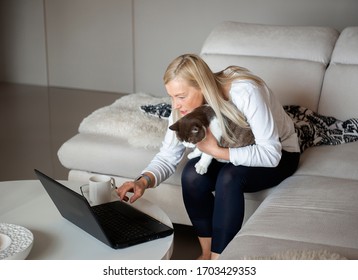 Mature Woman Holding Cat And Working On Laptop At Home On The Couch During A Corona Virus Pandemic In Krimulda,Latvia