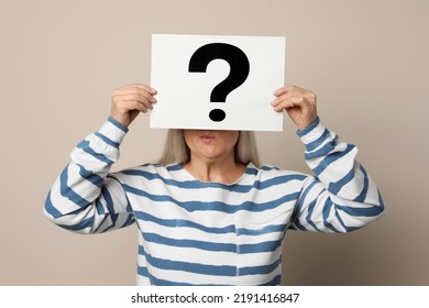 Mature Woman Holding Paper With Question Mark On Beige Background