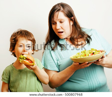 mature woman holding salad and little cute boy with hamburger teasing close up, family food, lifestyle real people concept