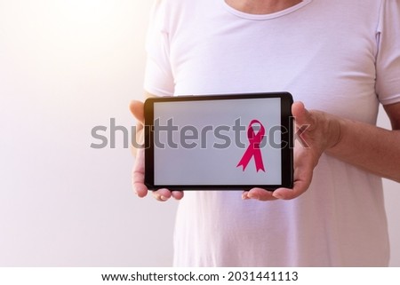 Mature woman holding tablet with a pink ribbon. Breast Cancer Awareness Month with tech image. 