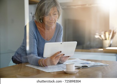 Mature Woman At Home Reading News On Digital Tablet