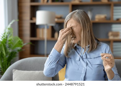 Mature woman at home touching her temples, feeling overwhelmed and stressed. She appears distressed and in need of comfort. - Powered by Shutterstock