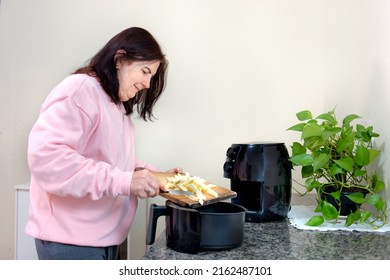 Mature Woman At Home Using An Air Fryer To Fry Sliced Potatoes. Making Healthy Food, Frying Without The Use Of Oil.