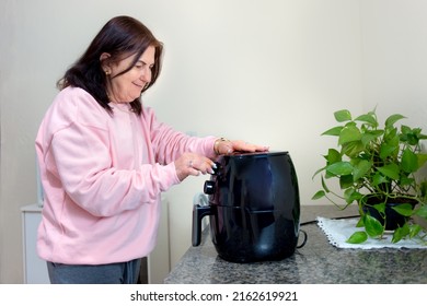 Mature Woman At Home Using An Air Fryer. Making Healthy Food, Frying Without The Use Of Oil.