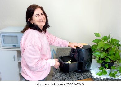 Mature Woman At Home Using An Air Fryer To Fry Sliced Potatoes. Making Healthy Food, Frying Without The Use Of Oil.