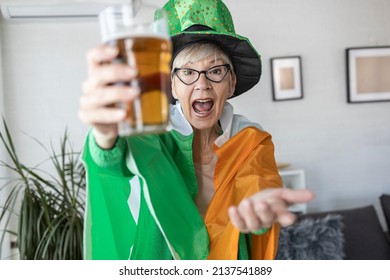 Mature Woman With Irish Flag On Shoulders Holding Glass Of Beer And Celebrate Saint Patrick Day