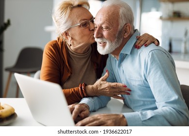 Mature woman kissing her mature husband while he uses a computer at home - Powered by Shutterstock