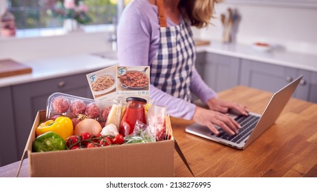 Mature Woman In Kitchen With Laptop To Find Recipe For Online Meal Food Kit Delivered To Home