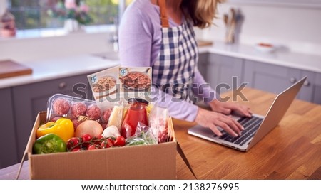 Mature Woman In Kitchen With Laptop To Find Recipe For Online Meal Food Kit Delivered To Home