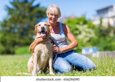 Mature Woman With A Labrador Retriever Sitting On The Lawn